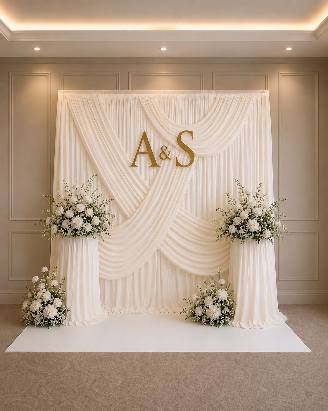 Ivory draped backdrop with gold initials and white floral arrangements
