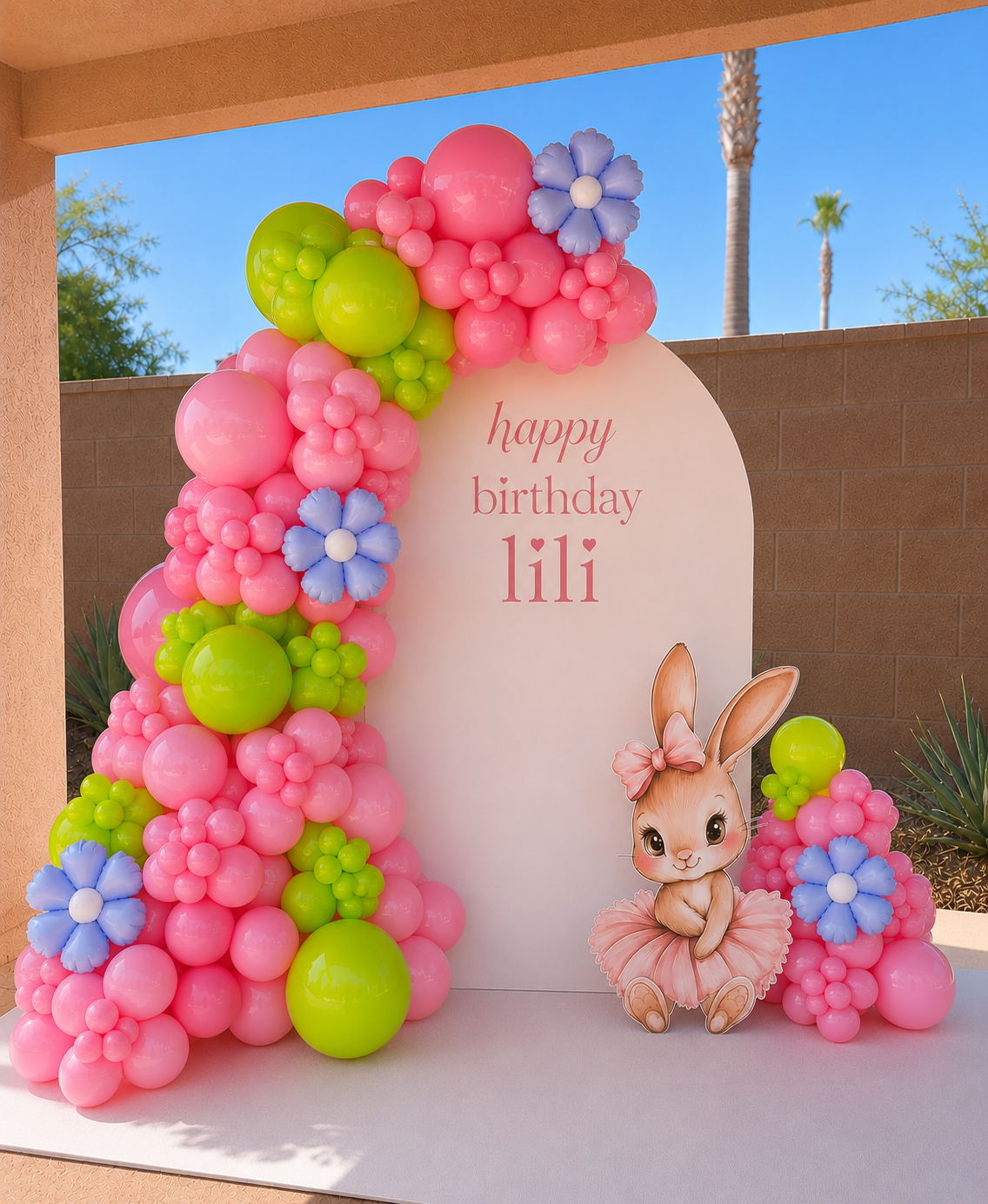 Pink, green and lavender balloons with balloon flowers and a bunny beside a birthday backdrop